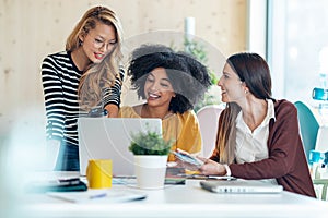 Casual multiethnic business women working with laptops while talking of they new projects together in coworking place