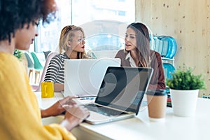 Casual multiethnic business women working with laptops while talking of they new projects together in coworking place