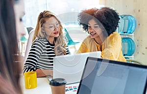 Casual multiethnic business women working with laptops while talking of they new projects together in coworking place