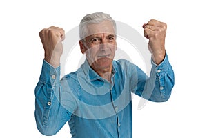 Casual old guy in denim shirt holding fists in the air and cheering victory