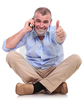 Casual old man sits and shows ok while on phone