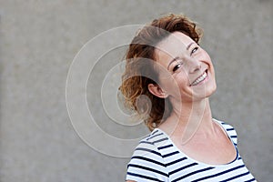 Casual older woman standing by wall smiling