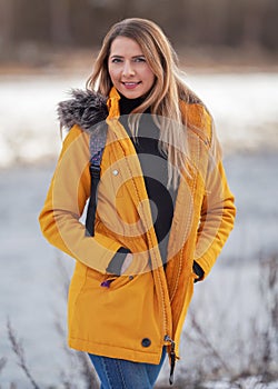 Casual portrait of young woman in warm orange yellow winter jacked, zipper down, smiling, blurred background behind her