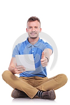 Casual seated young man with tablet shows thumb up