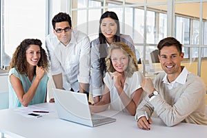 Casual smiling business team having a meeting using laptop