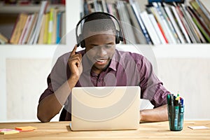 Casual smiling office worker in headphones looking at laptop scr