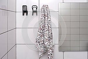 Casual towel is hanging on a unusual hook chair shape, bathroom interior with white tile and a mirror
