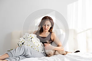 Casual woman with flowers and her Siamese cat in bedroom with flowers. life with pet. shadows