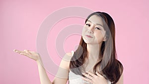 Casual woman presenting copy space on pink background. Portrait of pretty girl advertise product with hand gesture in studio