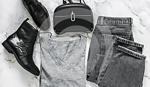 Casual women`s clothing set - grey mom`s jeans, cashmere pullover, black boots, cross body black bag on a marble background, top