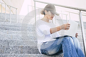 Casual young adult woman using laptop outdoor sitting on urban city stairs. New normal outside office workplace and digital online