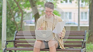 Casual Young Man Feeling Upset while Reading Contract and Using Laptop Outdoor