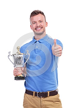 Casual young man with trophy shows thumb up