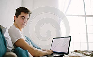 Casual young man using laptop in bed at home