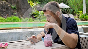 Casual Young Man Using Smartphone, Checking Mails, News Online, Drink Smoothie