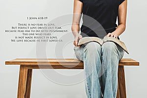 Casual young woman holds an open Bible 1 john 4:18-19 on her lap