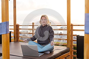 Casual young woman meditating on the empty beach with laptop. Freelance, time management concept. Stress at Work. Space