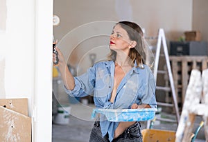 Casual young woman painting walls with a paint roller in refurbished room