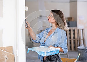 Casual young woman painting walls with a paint roller in refurbished room