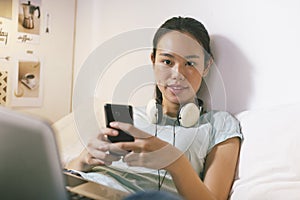 Casual young woman sitting on bed and using smart phone at home.