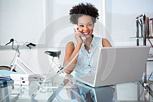 Casual young woman using telephone and laptop