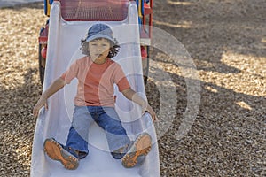 A casually dressed little boy looks at the camera when he reaches the bottom of the slide