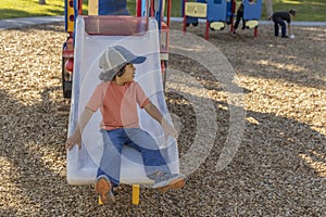 A casually dressed little boy looks to his left when he reaches the bottom of the slide