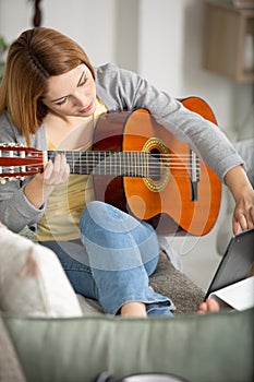 Casually dressed woman holding guitar and touching tablet screen