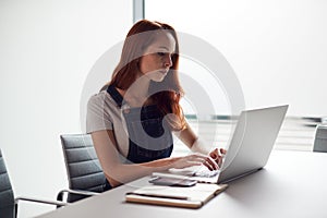 Casually Dressed Young Businesswoman Working On Laptop At Desk In Modern Workplace