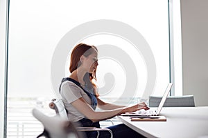 Casually Dressed Young Businesswoman Working On Laptop At Desk In Modern Workplace