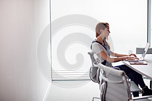 Casually Dressed Young Businesswoman Working On Laptop At Desk In Modern Workplace