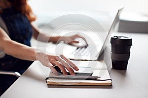 Casually Dressed Young Businesswoman Working On Laptop In Modern Office Picking Up Mobile Phone