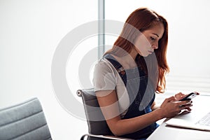 Casually Dressed Young Businesswoman Working On Laptop In Modern Workplace Checking Text Messages