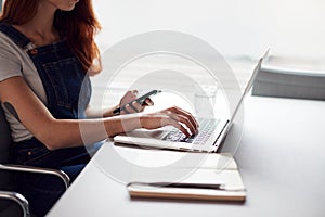 Casually Dressed Young Businesswoman Working On Laptop In Modern Workplace Checking Text Messages