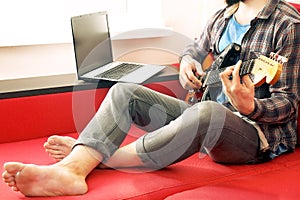 Casually dressed young man with guitar playing songs in the room at home. Online guitar lessons concept. Male guitarist practicing