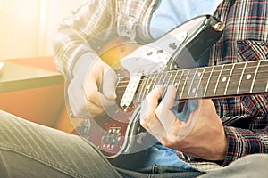 Casually dressed young man with guitar playing songs in the room at home. Online guitar lessons concept. Male guitarist practicing