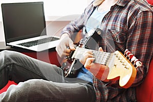 Casually dressed young man with guitar playing songs in the room at home. Online guitar lessons concept. Male guitarist practicing