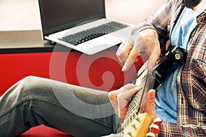 Casually dressed young man with guitar playing songs in the room at home. Online guitar lessons concept. Male guitarist practicing