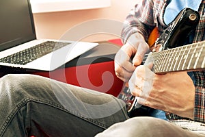 Casually dressed young man with guitar playing songs in the room at home. Online guitar lessons concept. Male guitarist practicing