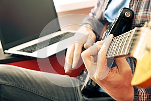 Casually dressed young man with guitar playing songs in the room at home. Online guitar lessons concept. Male guitarist practicing