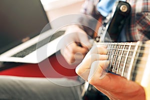 Casually dressed young man with guitar playing songs in the room at home. Online guitar lessons concept. Male guitarist practicing