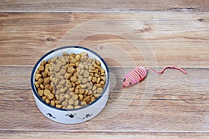 Cat dry food in a bowl and toy mouse. On brown wooden background