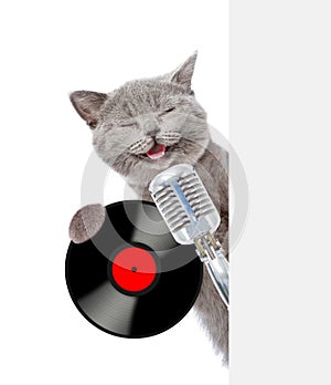 Cat holds retro microphone with vinyl record and peeking from behind empty board. isolated on white background