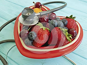 Cat homeless eats on the delicious strawberry, antioxid sweet blueberry, cherry, apricot plate heart on blue wooden, stethoscope