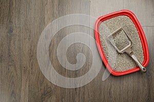 Cat litter tray with filler and scoop on wooden floor, top view. Space for text