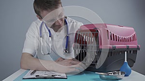 Cat in pet carrier on examination table of veterinarian clinic with pet doctor. Male veterinarian in white medical suit