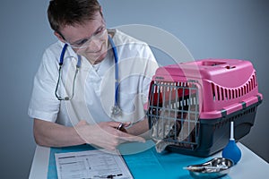 Cat in pet carrier on examination table of veterinarian clinic with pet doctor. Male veterinarian in white medical suit