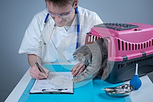 Cat in pet carrier on examination table of veterinarian clinic with pet doctor. Male veterinarian in white medical suit