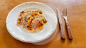 Catado de siri: brazilian food made of crab meat in a white plate with a fork and knife on a wooden background.