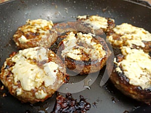 Catalimized onion beef burger with pickled onion and chive cheddar cheese cooking in a non stick pan